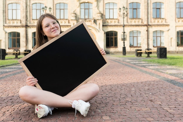 Vista frontale che si siede lavagna della holding della ragazza della high school