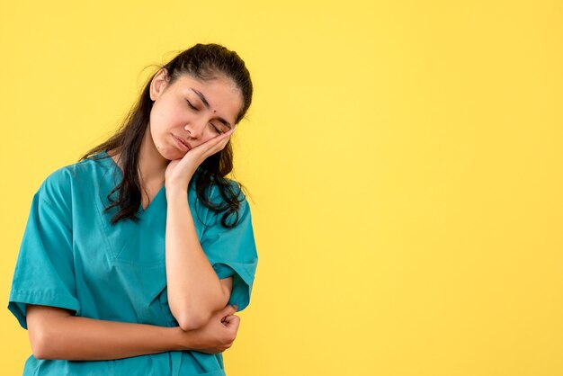 Front view sleepy female doctor in uniform standing on yellow background