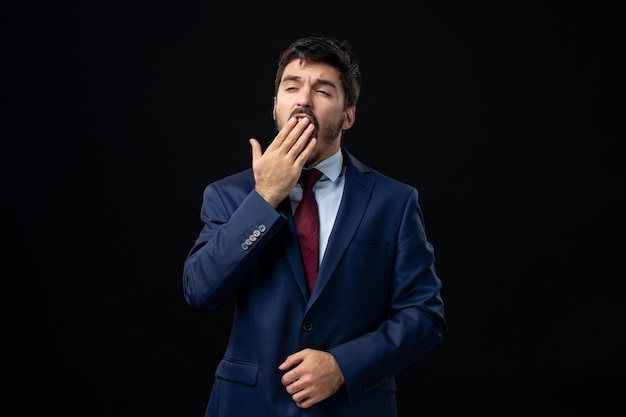 Front view of sleepy and young bearded man yawning on isolated dark wall