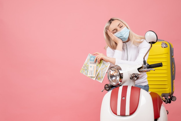 Front view sleepy young lady on moped with yellow suitcase holding map and ticket