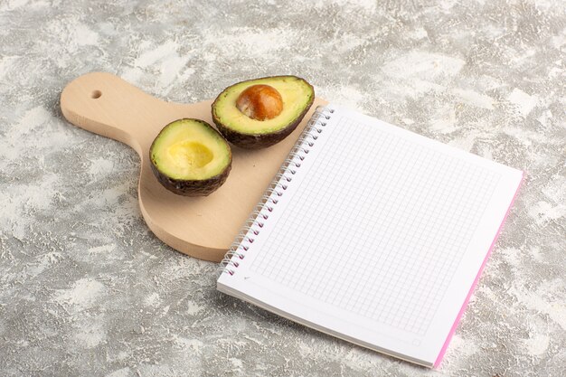 Front view sliced avocado with notepad on white desk