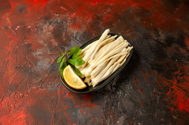Formaggio affettato vista frontale con pezzo di limone all'interno del piatto su foto di frutta color snack pasto scuro
