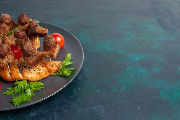 Front view sliced cooked meat with greens and cherry tomatoes inside plate on the dark blue surface