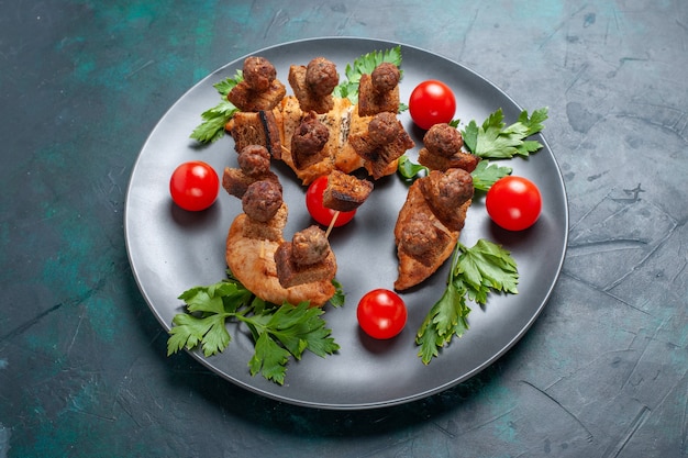 Front view sliced cooked meat with greens cherry tomatoes inside plate on dark-blue surface