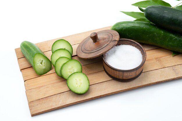 A front view sliced cucumbers with whole cucumbers and salt on brown wooden desk and white food meal