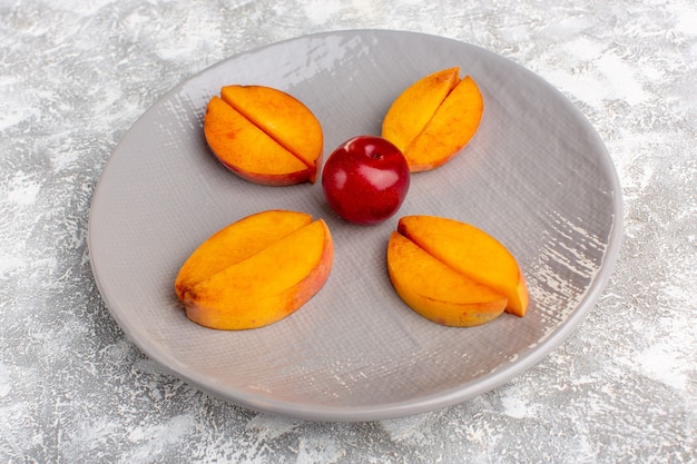 Front view sliced fresh peaches inside plate lined on the light white desk.