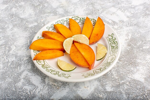 Вид спереди нарезанные свежие персики внутри тарелки с лимонами на светлом белом столе.