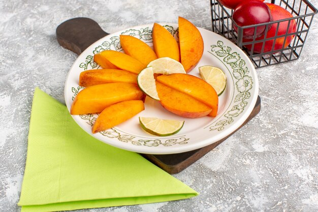 Front view sliced fresh peaches inside plate with lemons on light white floor fresh peach fruit mellow juice