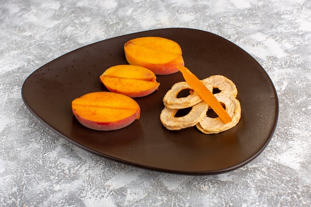 Front view sliced fresh peaches inside plate with pineapple rings on the light white desk.