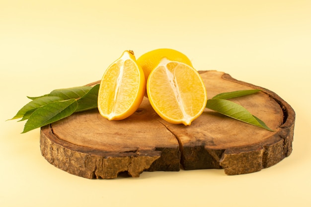 A front view sliced lemon and whole with green leaves on the wooden brown desk isolated fresh juicy mellow on the cream