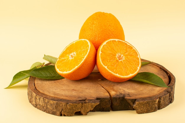 A front view sliced orange and whole with green leaves on the wooden brown desk isolated fresh juicy mellow on the cream