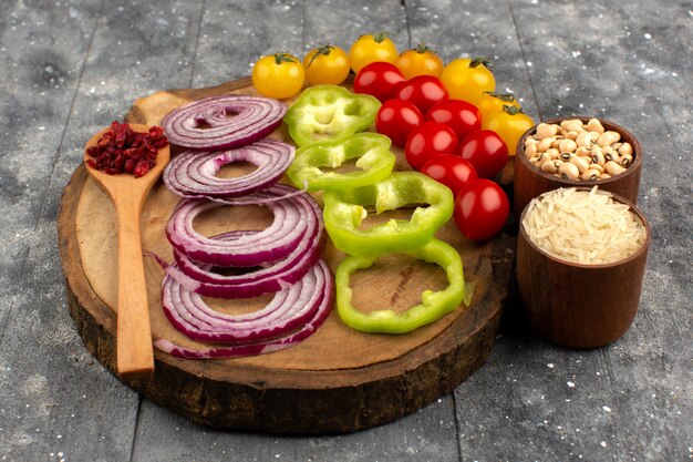 front view sliced vegetables such as onions green bell peppers yellow and red tomatoes on the brown desk and grey