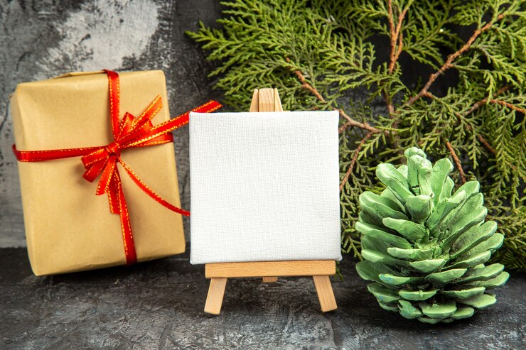 Free Photo front view small gift tied with red ribbon mini canvas on wooden easel pine branch on grey background