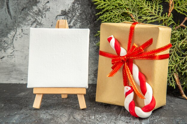 Front view small gift tied with red ribbon xmas candy mini canvas on wooden easel pine branch on grey