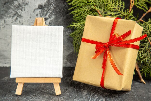 Front view small gift tied with red ribbon xmas candy mini canvas wooden easel pine branch on grey