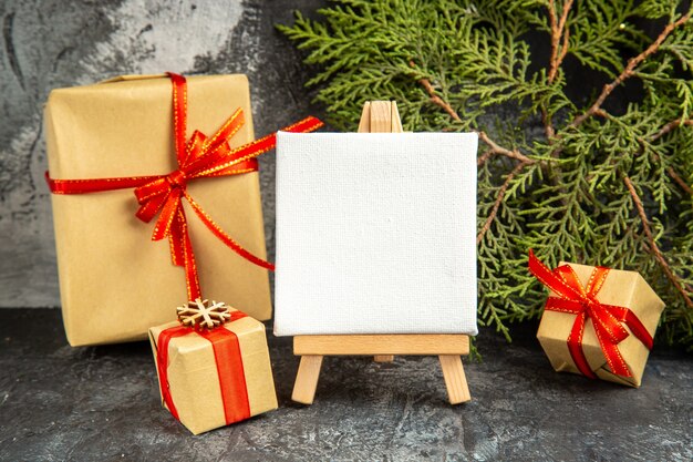 Front view small gifts tied with red ribbon mini canvas on wooden easel pine branch on grey background