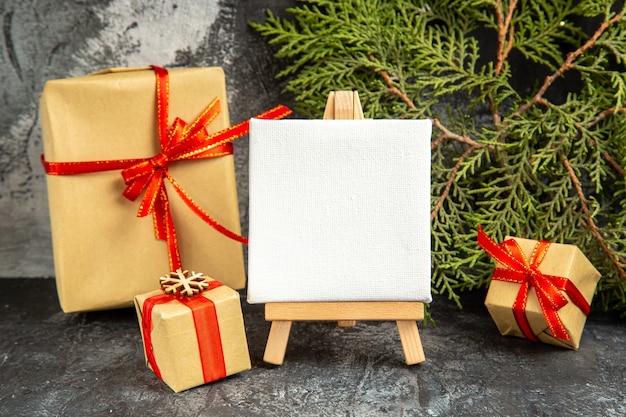 Front view small gifts tied with red ribbon mini canvas on wooden easel pine branch on grey background