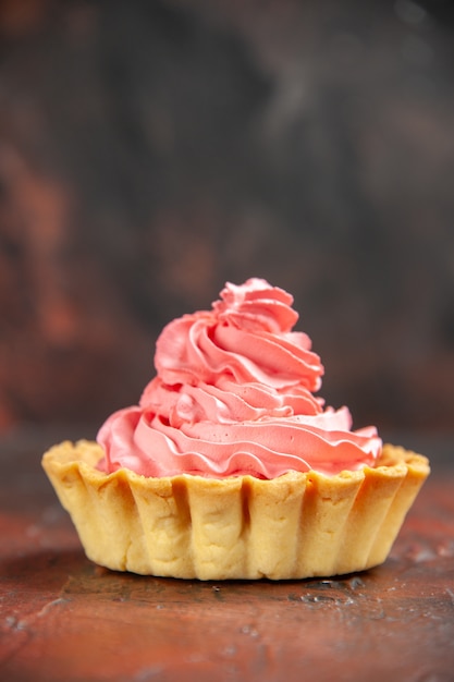 Небольшой пирог с розовым кондитерским кремом на темно-красном изолированном столе, вид спереди