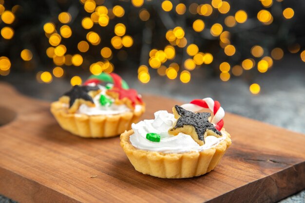 Front view small tarts on serving board on dark isolated surface xmas lights