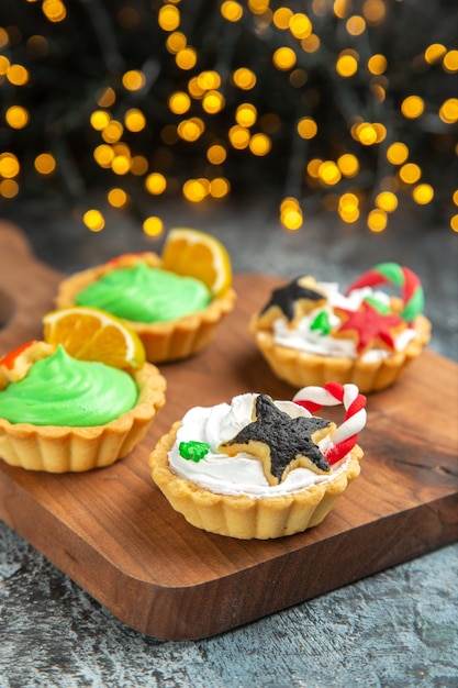 Front view small xmas tarts on cutting board on dark isolated surface xmas lights