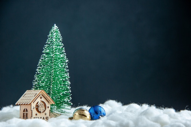 Вид спереди маленькая рождественская елка небольшой деревянный дом рождественские елочные шары на темной поверхности