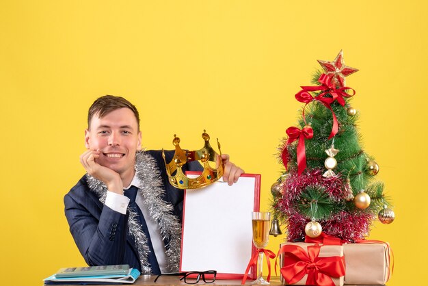 クリスマスツリーの近くのテーブルに座って、黄色でプレゼント笑顔のハンサムな男の正面図
