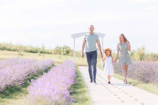 Front view of smiled parents holding hands of daughter, walking on path in sunny day