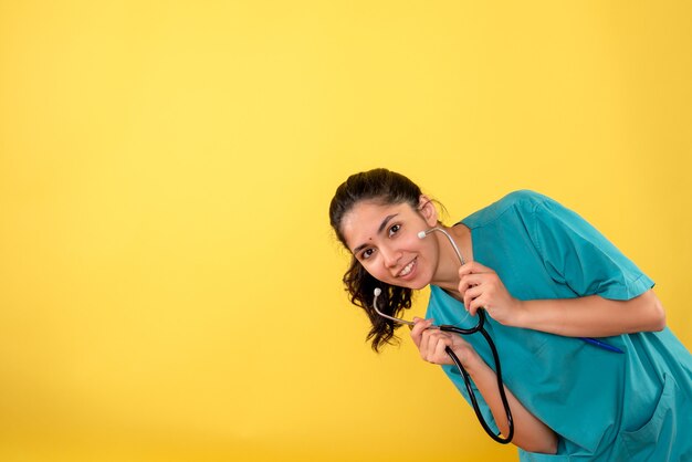 Vista frontale sorrise giovane medico femminile che tiene lo stetoscopio su sfondo giallo
