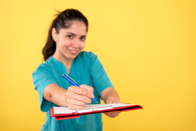 Front view smiled young female holding clipboard on yellow background