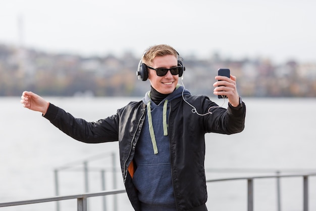 Front view smiley blonde man listening to music outdoors