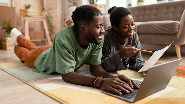 Vista frontale della coppia sorridente sul pavimento facendo piani per ridipingere la casa con il computer portatile