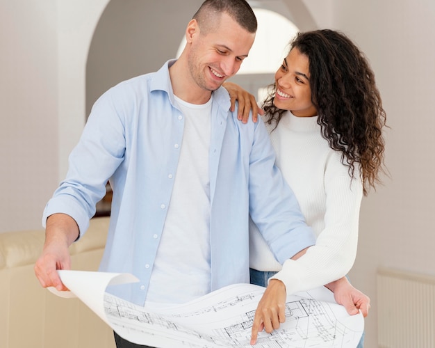 Front view of smiley couple holding house plans
