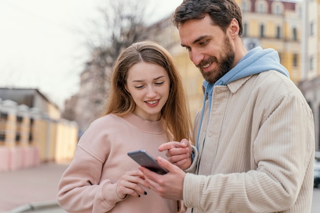 スマートフォンを使用して街の屋外で笑顔のカップルの正面図