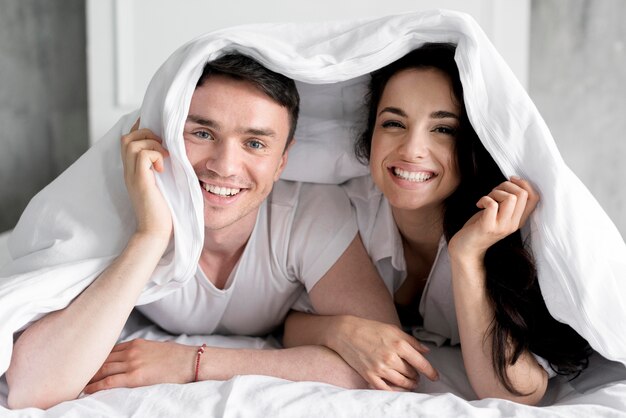頭の上に毛布が付いているベッドでポーズをとってスマイリーカップルの正面図
