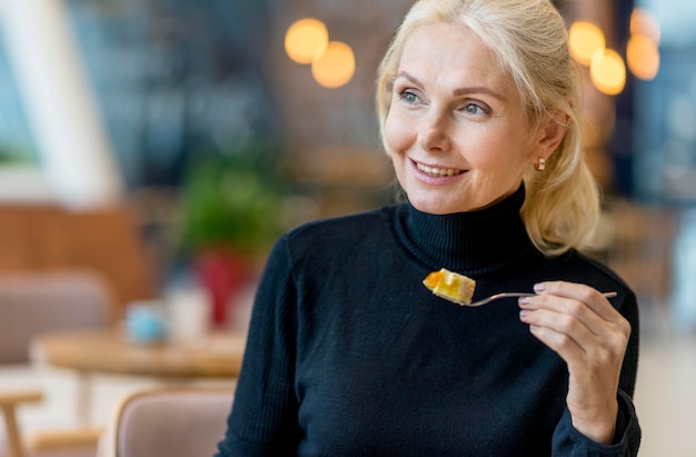 Vista frontale della donna di affari dell'anziano di smiley che mangia dessert mentre lavora