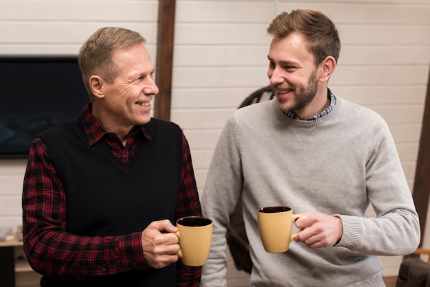 Free photo front view smiley father and son posing while holding cups