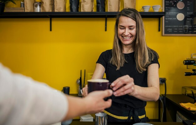 Front view of smiley female barista handing cup of coffee