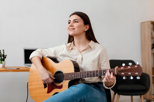어쿠스틱 기타를 연주하는 웃는 여성 음악가의 전면보기