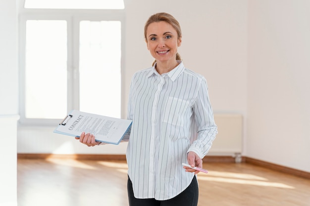 Free photo front view of smiley female realtor in empty house holding clipboard