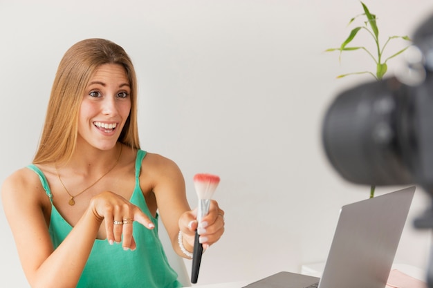 Front view smiley female showing makeup brush to camera