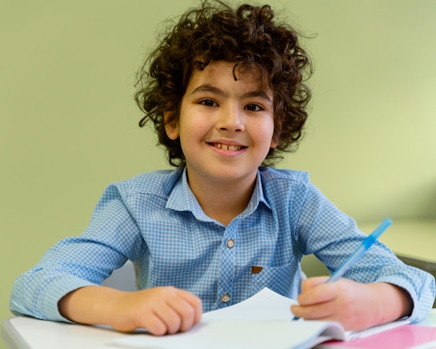 Foto gratuita vista frontale del ragazzino sorridente in classe a scuola