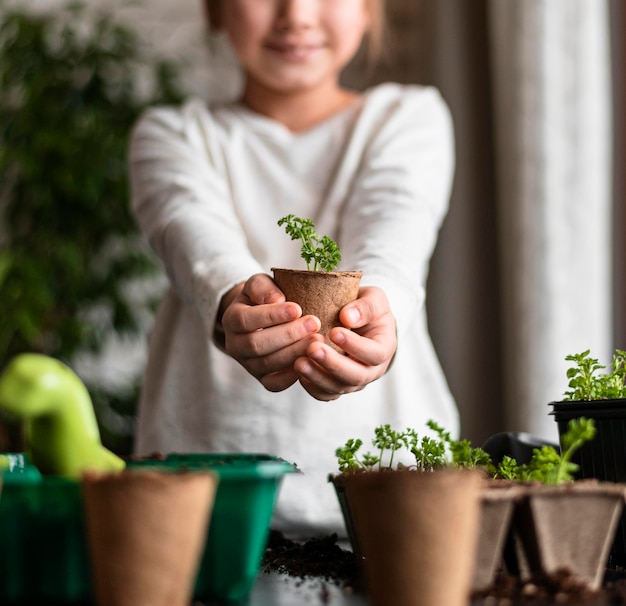 Front view of smiley little girl holding plant in pot at home
