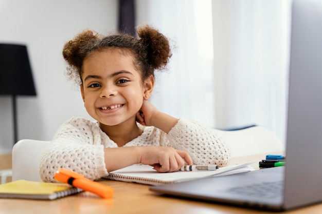 ノートパソコンでオンライン学校の間に自宅で笑顔の小さな女の子の正面図