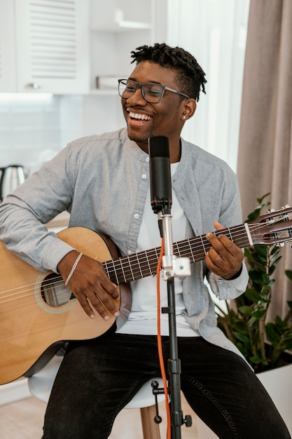 Front view of smiley male musician at home playing guitar and singing