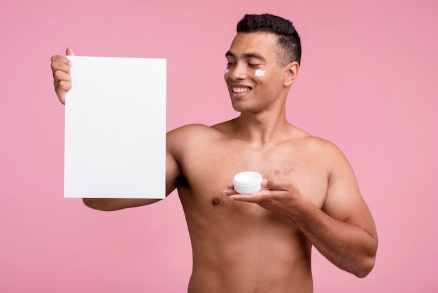 Front view of smiley man holding face cream and blank placard