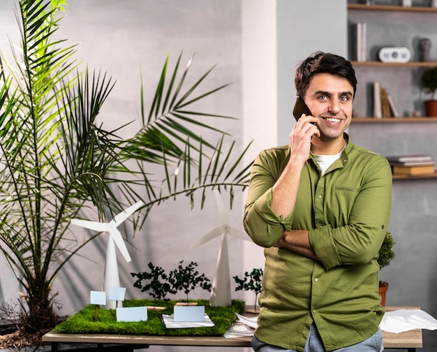 Front view of smiley man talking on the phone next to an eco-friendly wind power project layout