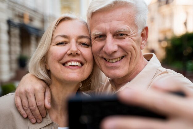 Front view of smiley senior couple taking a selfie while out in the city
