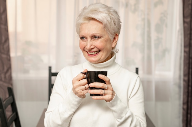 Front view smiley senior female holding cup of coffee