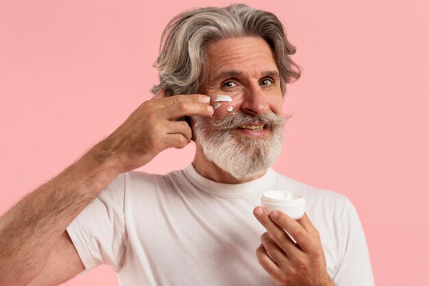 Front view of smiley senior man with beard applying cream