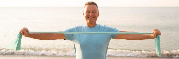 Free photo front view of smiley senior man working out with elastic rope on the beach